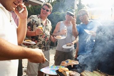 Man barbecuing using mobile phone, friends laughing in background