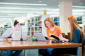 Group of young students studying in public library using laptop computers and reference books --- Image by © Peter M. Fisher/Corbis