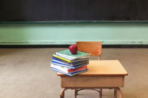 Stack of school books and apple on desk in empty classroom